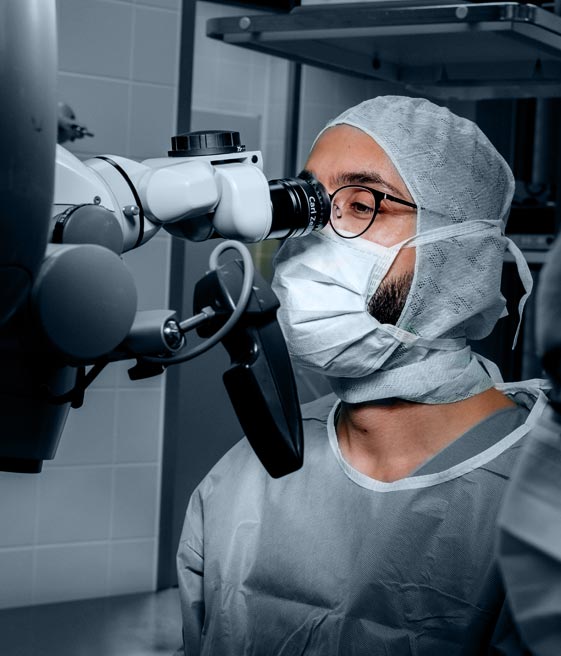 Dr. Kaveh Mehdiani schaut durch ein Operationsmikroskop in einem OP-Raum